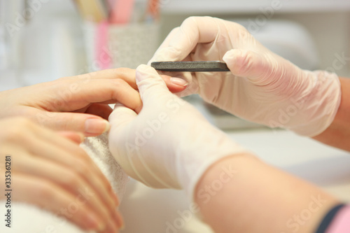 Closeup shot of a woman in a nail salon getting a manicure by a cosmetologist with a nail file. Woman gets a manicure of nails. Beautician puts nails on the client. 