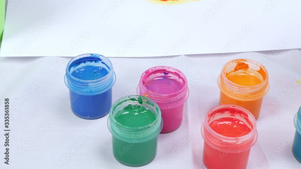 From above of opened jars with multicolored gouache paints on table with white paper sheet near From above of opened jars with multicolored gouache paints on table with white paper sheet near