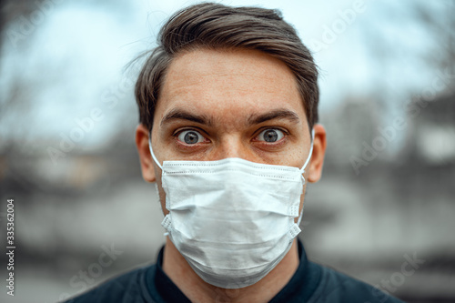 Portrait man in medical mask. Young man stands on light background and looking at camera.