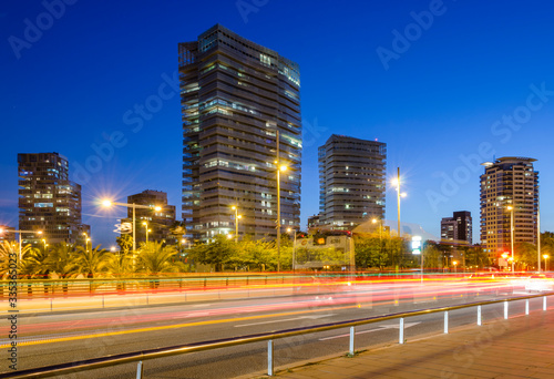 Paisaje urbano de los edificios de la ciudad de Barcelona al anochecer con calle en primer termino y las luces de los coches.