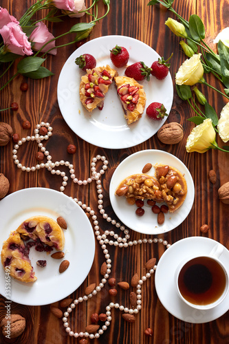 Cup of coffee and three cut mini tarts cupcakes with strawberries  blueberries and with walnuts  almonds and hazelnuts on plate. Top view