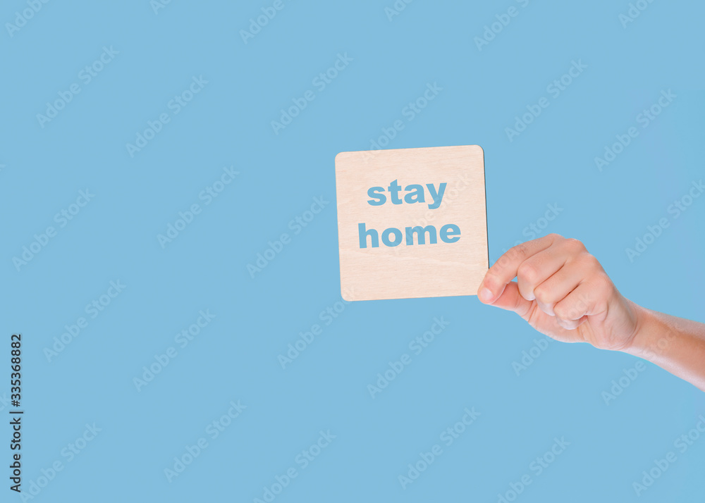 Hand holding a wooden blank with stay home on blue background Hand holding a wooden blank with stay home on blue background