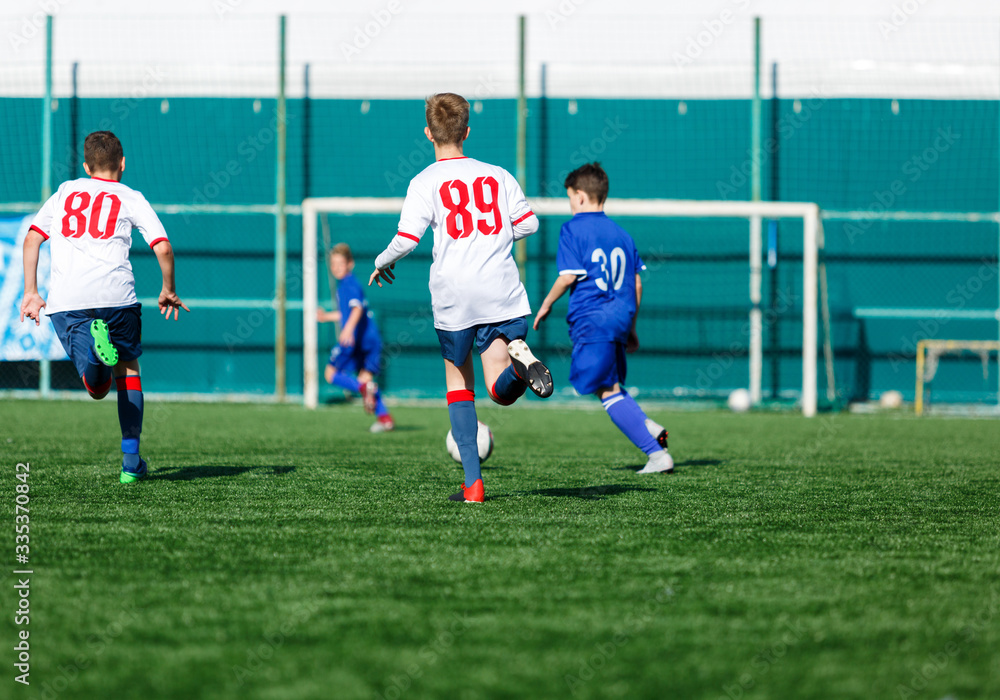 Boys in white and blue sportswear plays football on field, dribbles ball. Young soccer players with ball on green grass. Training, football, active lifestyle for kids concept Boys in white and blue sportswear plays football on field, dribbles ball. Young soccer players with ball on green grass. Training, football, active lifestyle for kids concept