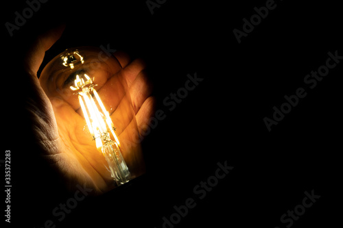 Invention, ideas and leadership concept; Close up glowing lighting bulb on dark black background.