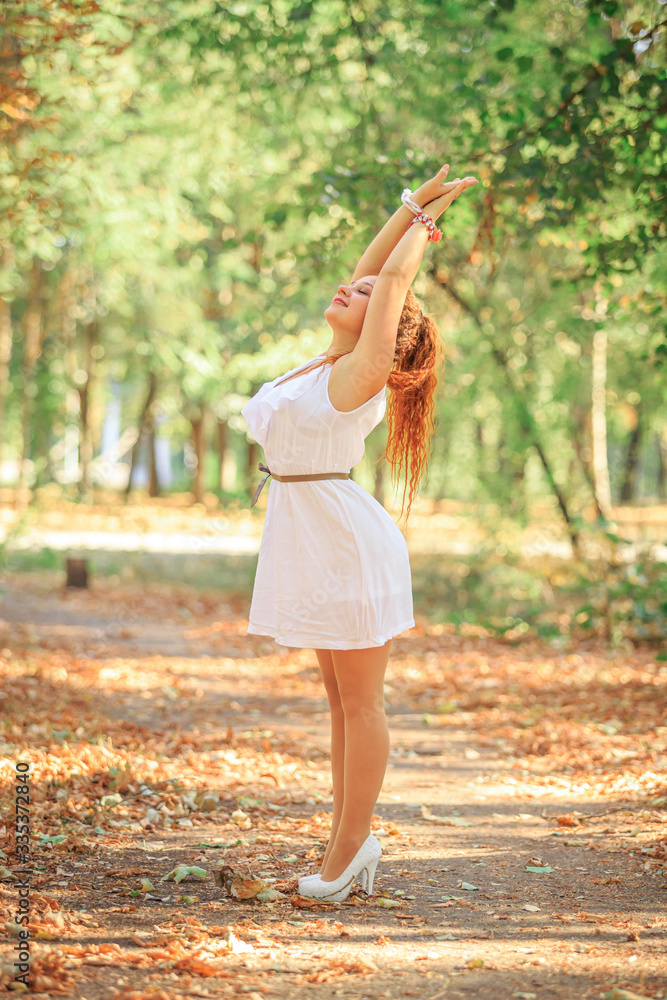 Red-haired girl in a white dress in the park in early autumn