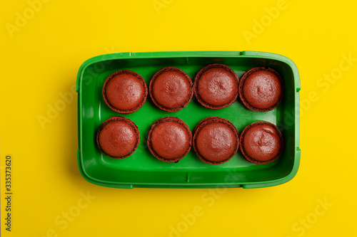 Brown macaroons in plastic box on yellow, top view, © Mikhail