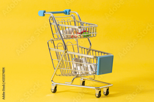 Small supermarket grocery push cart for shopping toy with wheels and groceries on yellow background