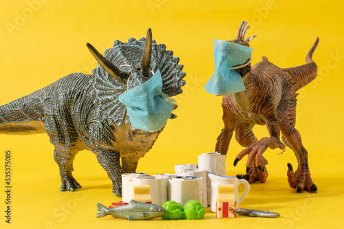 Photo Two plastic dinosaurs with face masks and groceries on yellow background