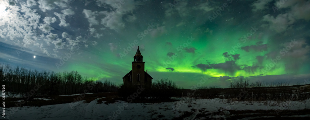 Aurora lighting up the night sky with shades of bright green behind and abandoned prairie church.  The sky includes stars and moon lit clouds. - obrazy, fototapety, plakaty 
