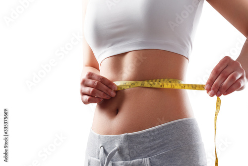 Close up of slim woman measuring her waist's size with tape measure.