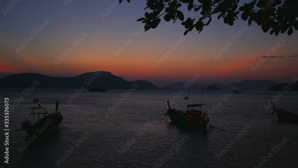 moving leaf branch tree, moving water wave sea, moving thai flag on parking long tail boat tied with long rope,silhouette mountain and island, in twilight orange color sky evening time after sunset moving leaf branch tree, moving water wave sea, moving thai flag on parking long tail boat tied with long rope,silhouette mountain and island, in twilight orange color sky evening time after sunset