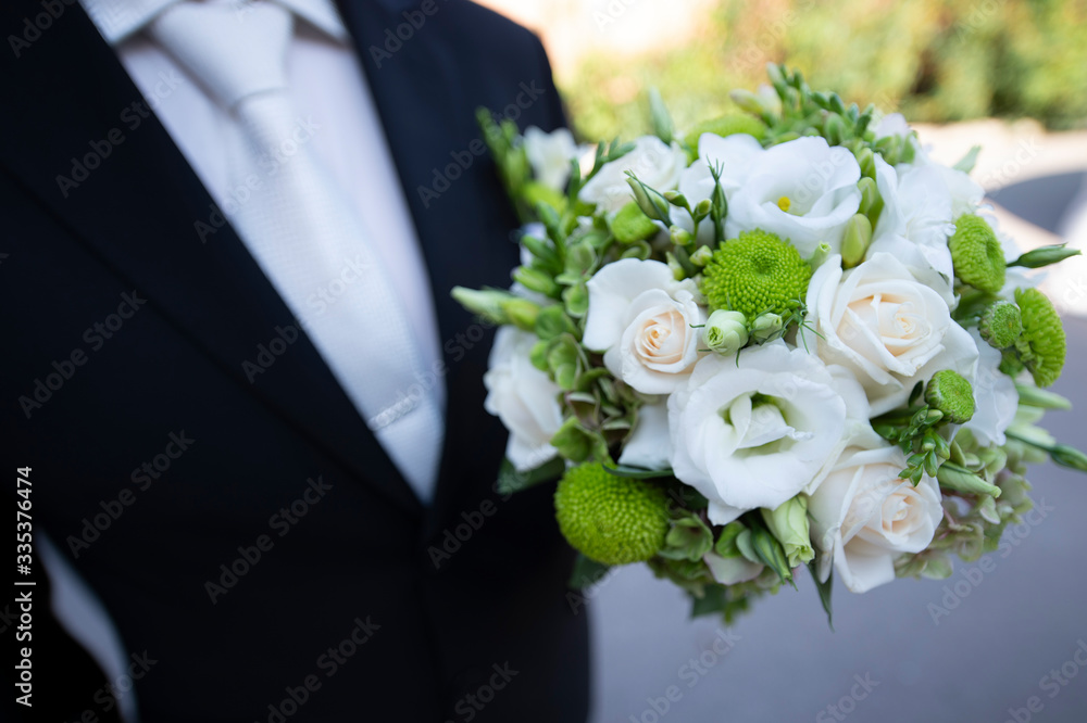 The groom holds a bouquet of white wedding flowers The groom holds a bouquet of white wedding flowers