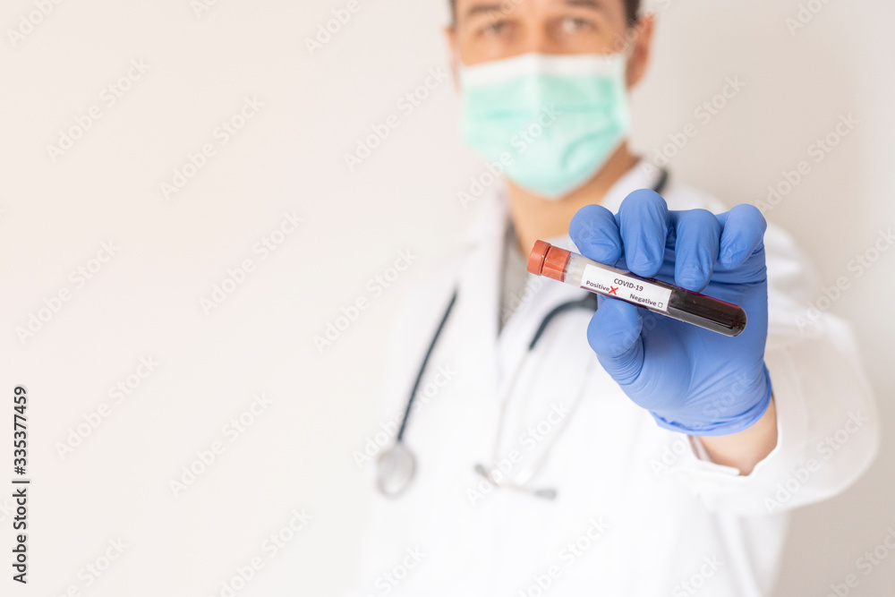Unfocused portrait of a scientist wearing a mask holding a test tube with a positive sample of coronavirus. Unfocused portrait of a scientist wearing a mask holding a test tube with a positive sample of coronavirus.