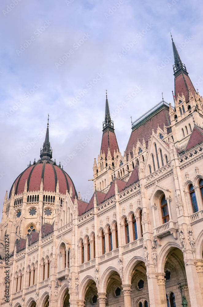 Building of the Hungarian Parliament Orszaghaz in Budapest, Hungary. The seat of the National Assembly. House built in neo-gothic style. Sunset light, pink and purple sky and clouds. Vertical photo