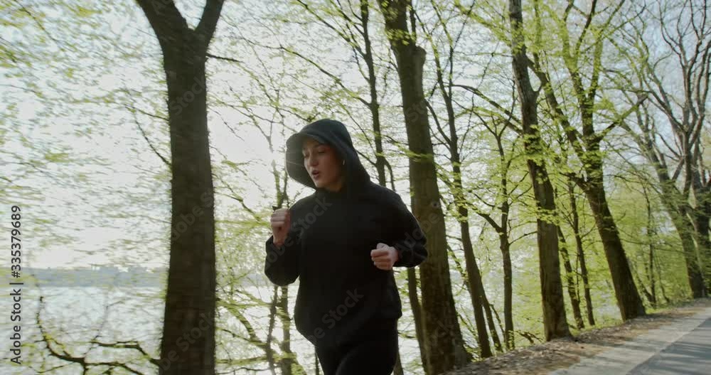 Woman in hoodie jogging in park Woman in hoodie jogging in park
