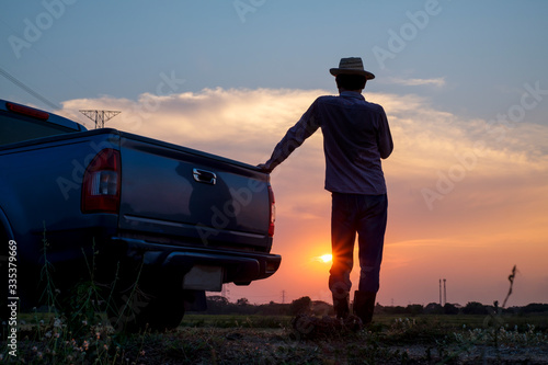 Rear view of male farmer standing looking at farmland at sunset, farm activity preparation, traveling by pickup truck