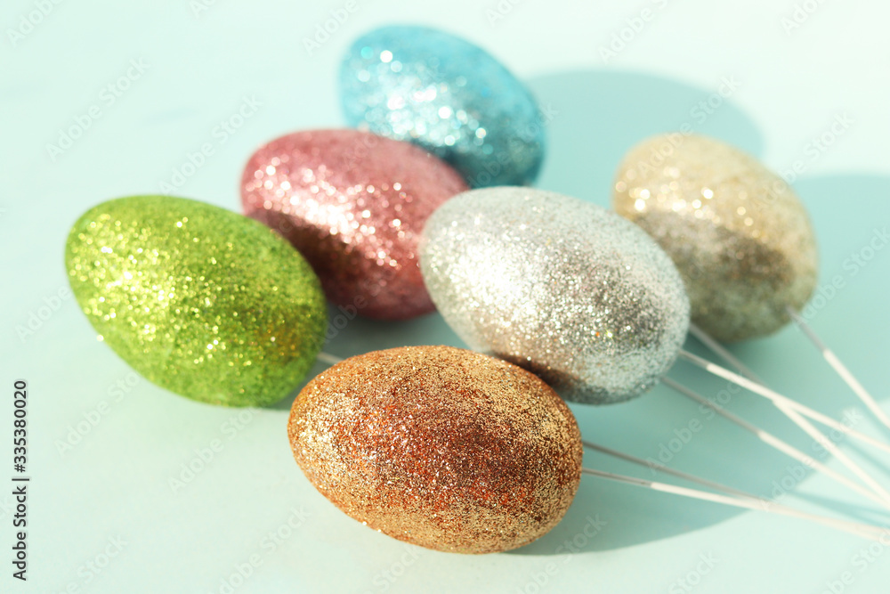 Shiny bright sparkling Easter eggs on sticks as a decoration on a blue background in the sun. Selective focus. Shiny bright sparkling Easter eggs on sticks as a decoration on a blue background in the sun. Selective focus.