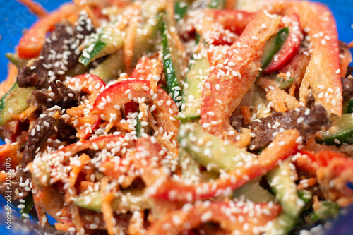 brightly colored vegetable salad with meat sprinkled with sesame seeds, close-up, blurred background