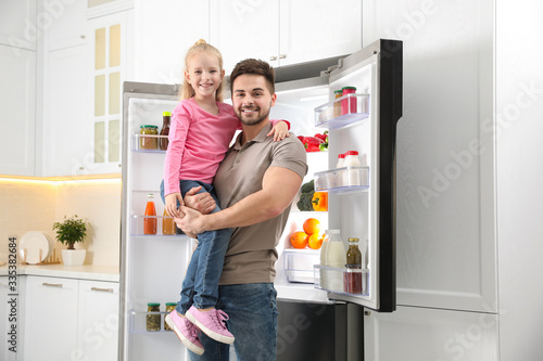 Young father with daughter near open refrigerator in kitchen