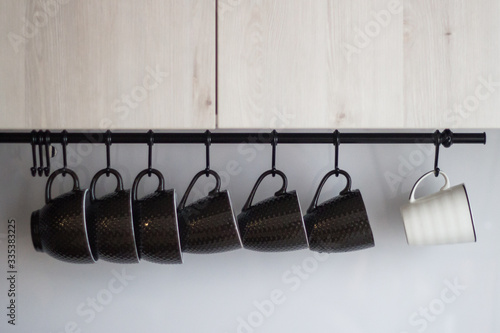 Several brown porcelain and one white mug hanging on hooks in gray-blue tones.

