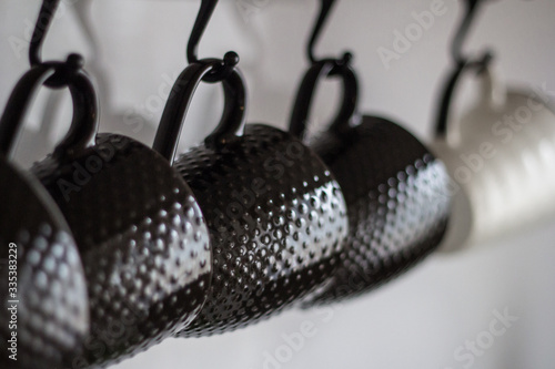 
Several brown porcelain and one white mug hanging on hooks with a close-up in the foreground and a blurry background in gray-blue tones.
