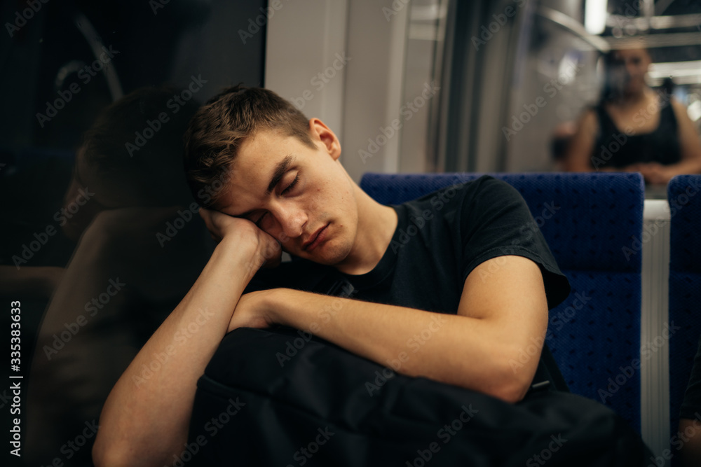 Passenger sitting in the seat and sleeping inside a train/bus while traveling.Tired exhausted looking young man getting away with train ride.Going home from work.Bored person during commute time.Nap