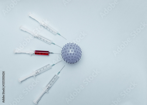On a blue background lies a ball in the form of a coronavirus infection, around which there are large syringes with drugs for injection. Epidemic. Pandemic. chrono white photo.