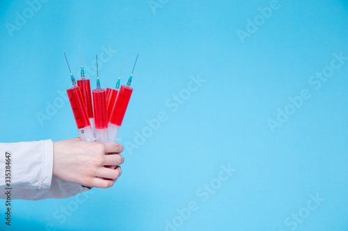 On a blue background in the hands of a girl who is dressed in a white Bicycle, a lot of large medical syringes with red injectable medicine. concept.