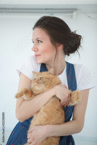 Young cute woman holding a red fluffy cat in her arms and smiling. Stay home. Cozy atmosphere