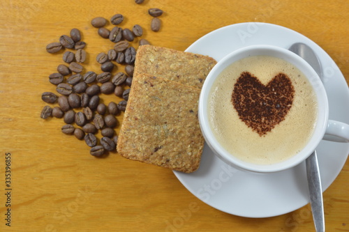 cup of coffee with a heart shape on it, coffee beans and a cookie, on a wooden table