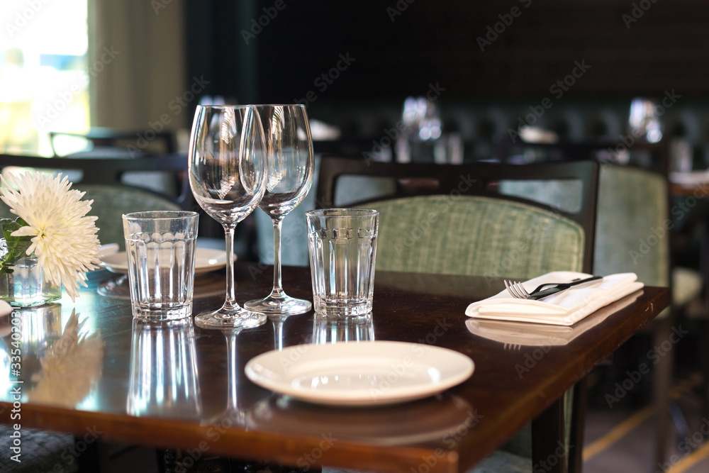 Glasses, flowers, fork, knife served for dinner in restaurant with cozy interior, retro film filter effect Glasses, flowers, fork, knife served for dinner in restaurant with cozy interior, retro film filter effect