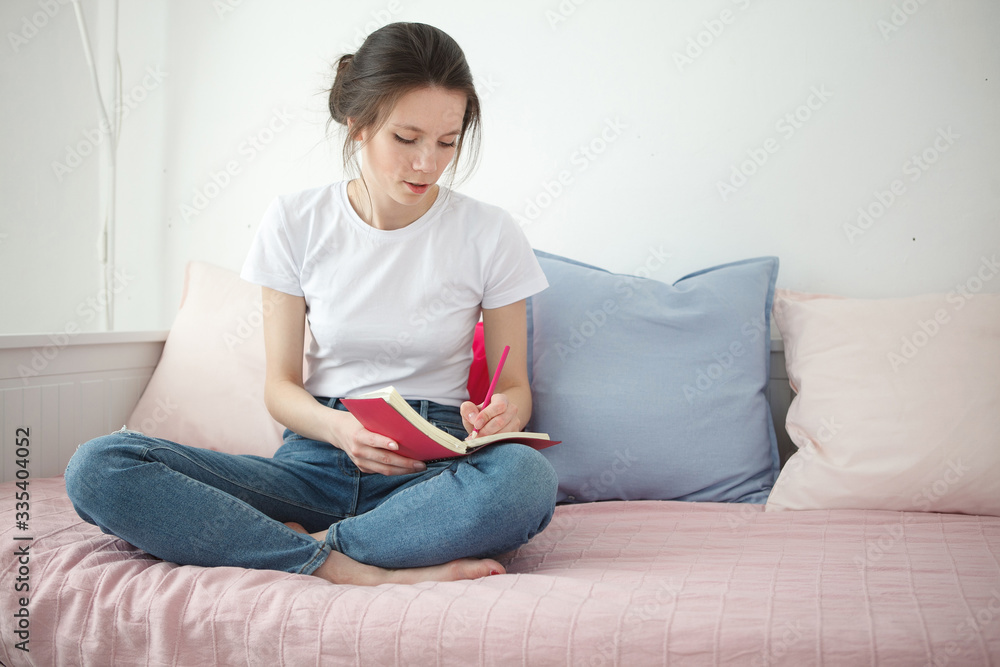 Young woman with notebook sitting on the bed. Peaceful atmosphere. Woman stay home during a quarantine. Home concept. Self isolation. Young woman with notebook sitting on the bed. Peaceful atmosphere. Woman stay home during a quarantine. Home concept. Self isolation.
