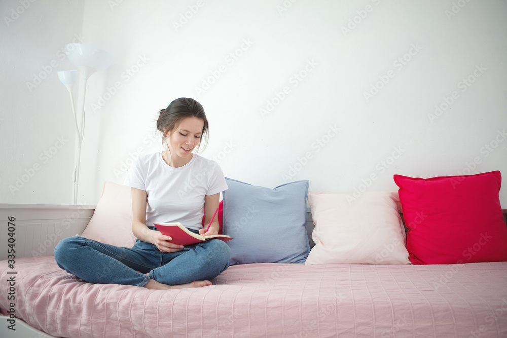 Young woman with notebook sitting on the bed. Peaceful atmosphere. Woman stay home during a quarantine. Home concept. Self isolation. Young woman with notebook sitting on the bed. Peaceful atmosphere. Woman stay home during a quarantine. Home concept. Self isolation.