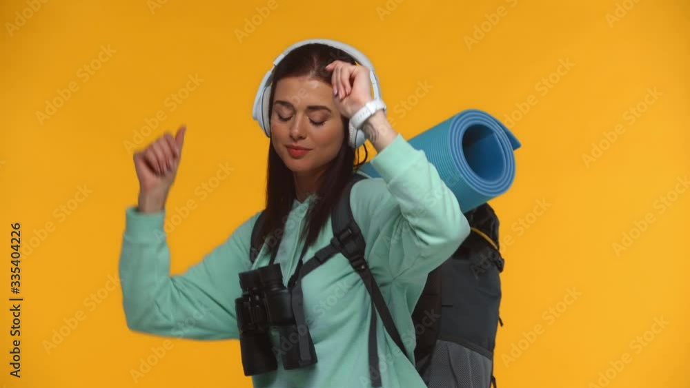 Tourist in headphones dancing and smiling at camera isolated on yellow Tourist in headphones dancing and smiling at camera isolated on yellow