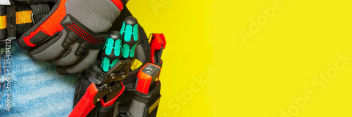 Fotografie Electrician or professional Builder in the installer's belt with tools on a yellow background