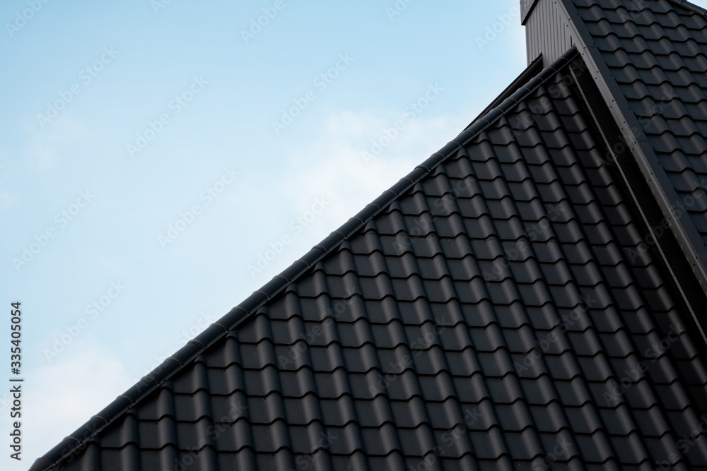 Black metal tile roof. Roof metal sheets. Modern types of roofing materials. Roof of the house, metal roof tile against the blue sky. Building. Black metal tile roof. Roof metal sheets. Modern types of roofing materials. Roof of the house, metal roof tile against the blue sky. Building.