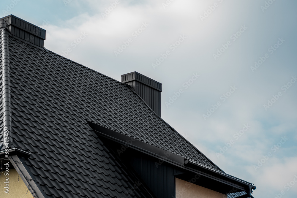 Black metal tile roof. Roof metal sheets. Modern types of roofing materials. Roof of the house, metal roof tile against the blue sky. Building.