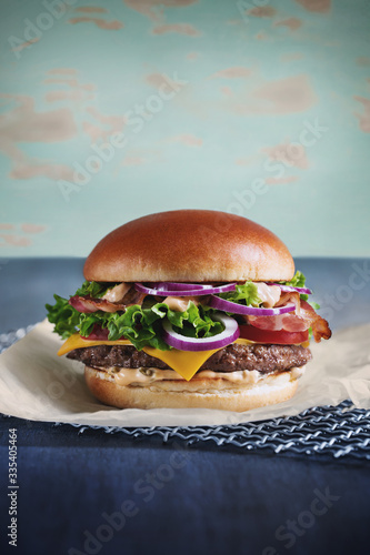 juicy burger with bacon, meat, onion sauce, herbs and tomato on parchment in a crispy bun