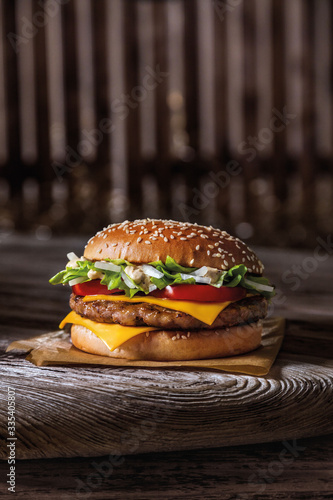 burger bun with sesame seeds, meat, cheese and on a wooden table and parchment, ready poster for printing