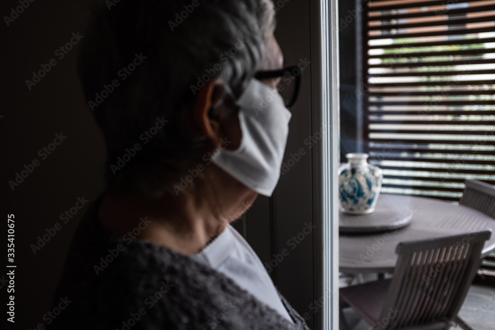 Blurry close-up of a senior adult wearing a protective mask and looking out the window.