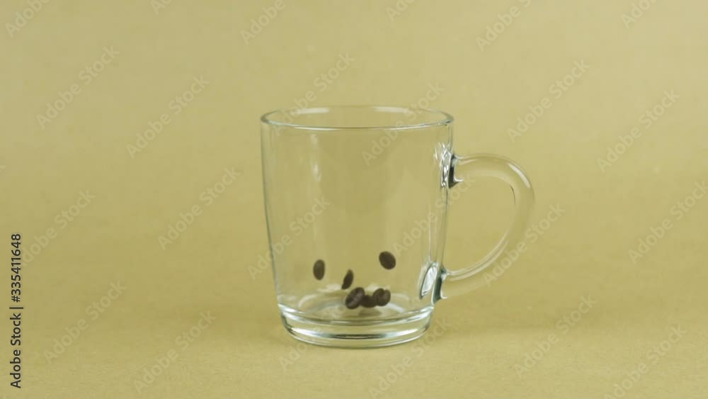 Coffee beans quickly fall, clear glass cup, beige background. Energy concept Coffee beans quickly fall, clear glass cup, beige background. Energy concept