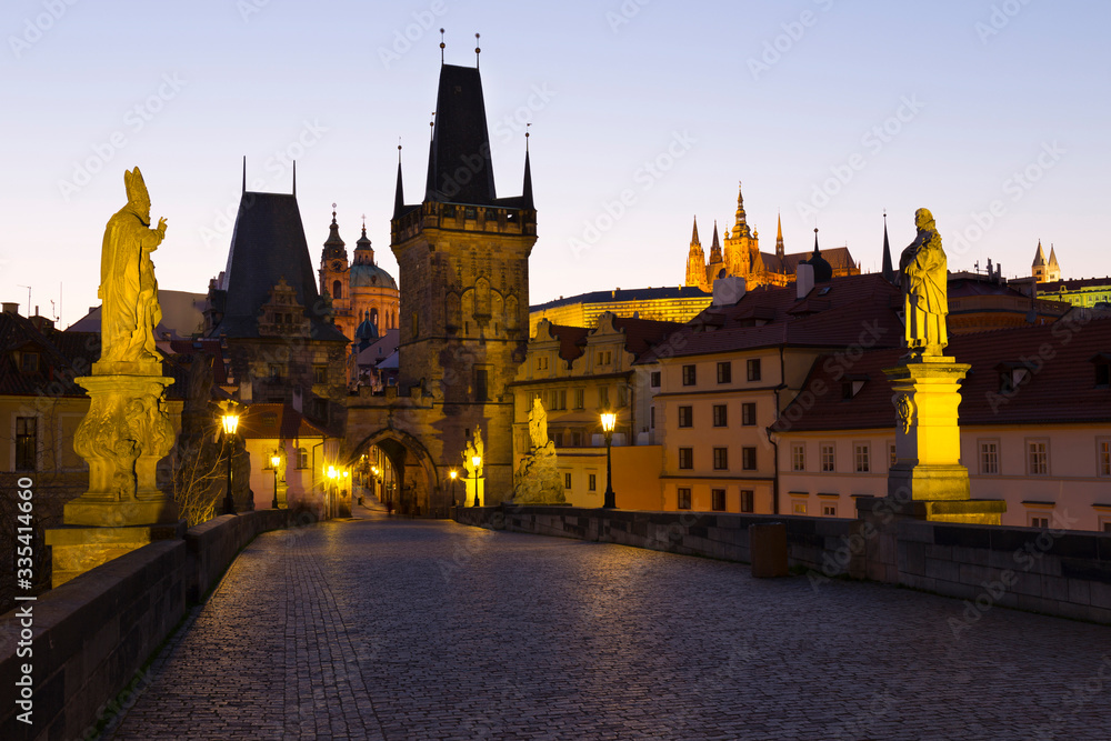Night colorful Prague gothic Castle with St. Nicholas' Cathedral and Bridge Tower from Charles Bridge with its baroque Statues without People at the time of Coronavirus, Czech Republic
