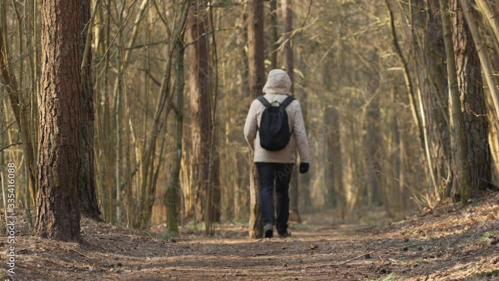 Back view of an adult man fast walking away in the forest. A guy in casual clothes with backpack and hood rushing on a calm quiet spring morning. Back view of an adult man fast walking away in the forest. A guy in casual clothes with backpack and hood rushing on a calm quiet spring morning.