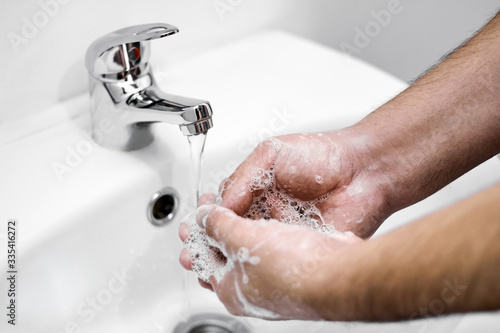 A man washes his hands with soap over a white sink as a prophylaxis against coronovirus infection COVID-19. Healthy skin without bacteria. Personal hygiene