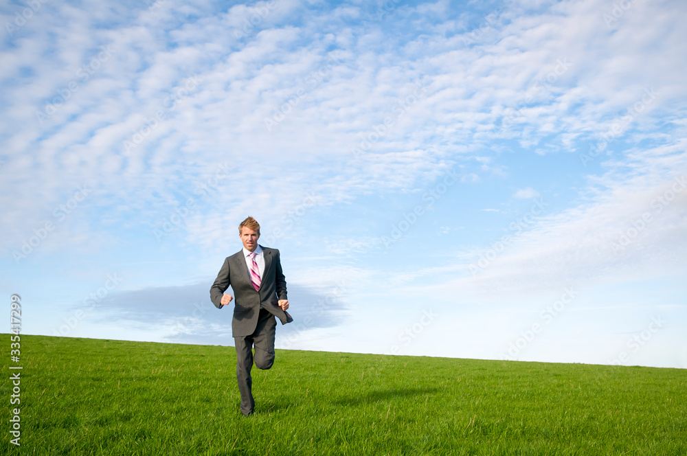Solitary businessman running across sloping green grass meadow Solitary businessman running across sloping green grass meadow