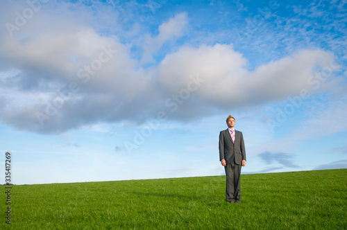 Lone businessman standing in the middle of a deserted green grass meadow