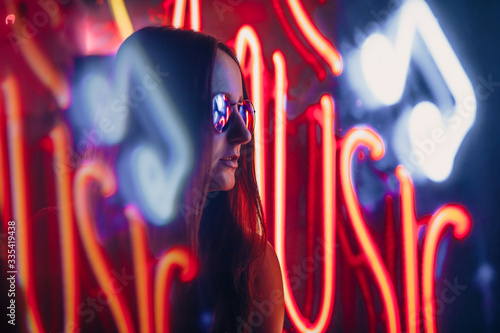 a girl in neon light with glasses in smoke near a nightclub. City street in neon light. Fashion girl model shooting at night in neon light.
