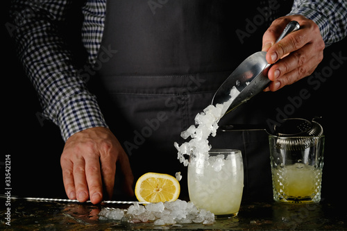 The process of making a refreshing cocktail with ice.The bartender is pouring ice into a glass.