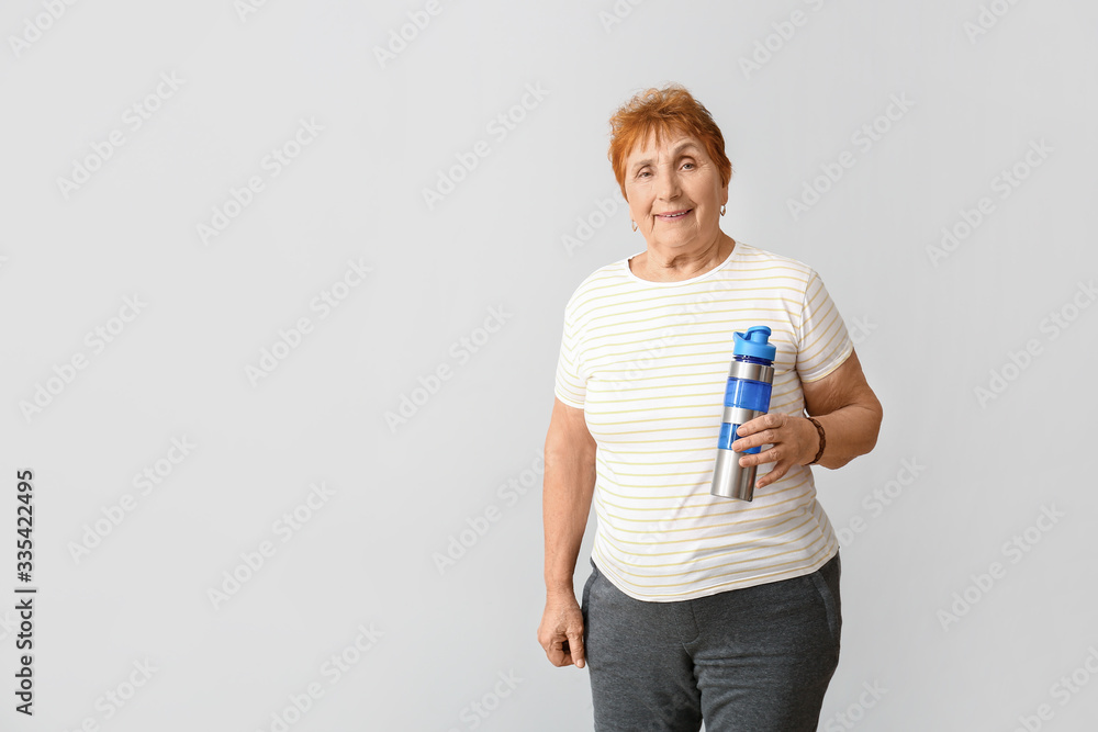 Elderly woman with bottle of water on light background Elderly woman with bottle of water on light background
