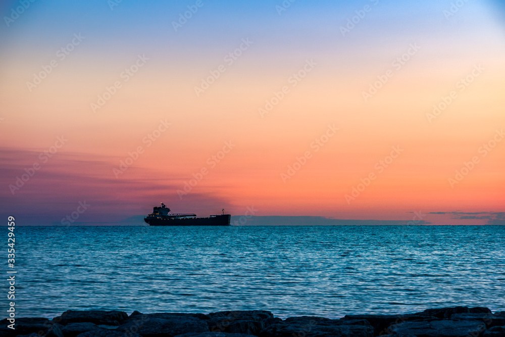 Tanker ship coming into harbor, on a background of sunset sky